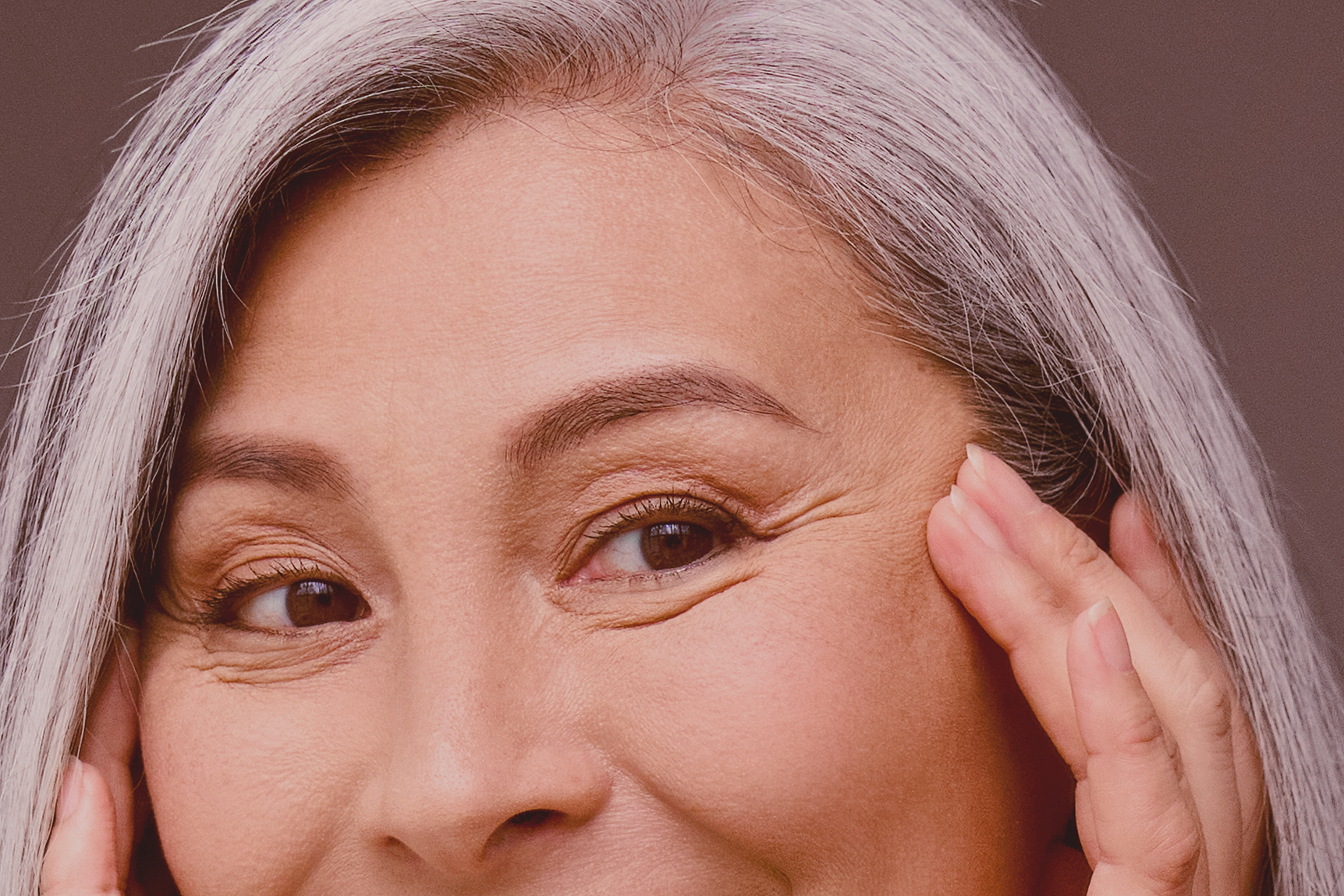 Happy middle 50 years aged asian woman with gray hair looking at mirror reflection examining touching face enjoying antiaging beauty treatments.